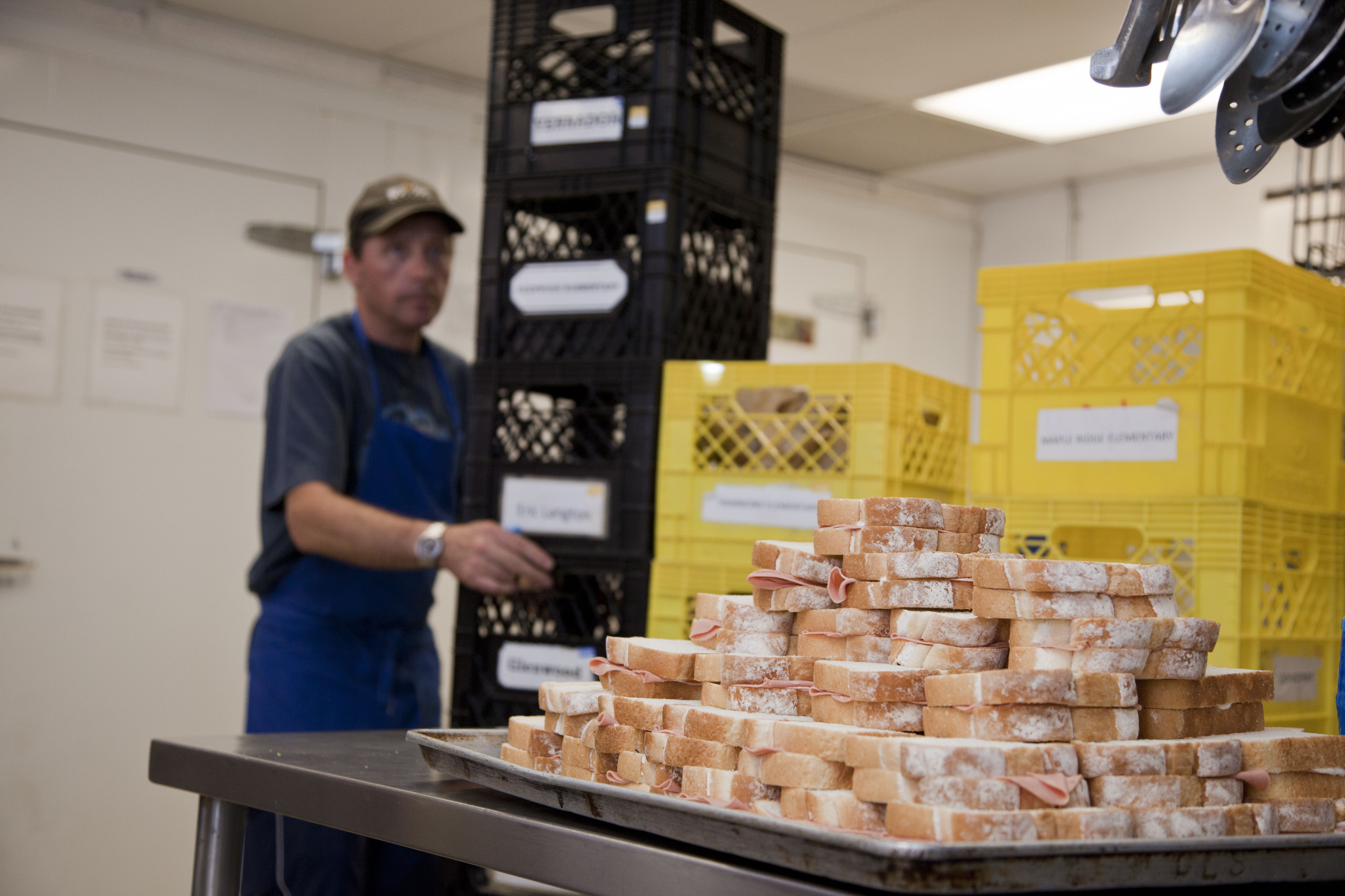 Person standing beside a table stacked with prepared sandwiches in a kitchen.
