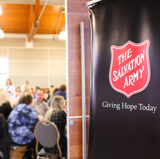 The Salvation Army shield banner displayed indoors with people seated in the background.