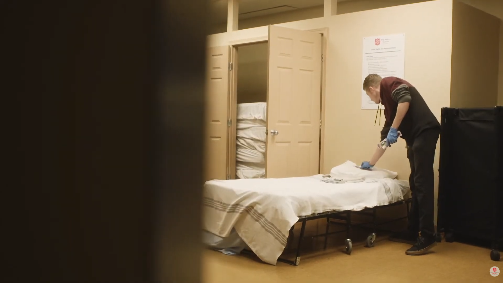 A staff member preparing a bed with fresh linens inside the Salvation Army temporary winter shelter.